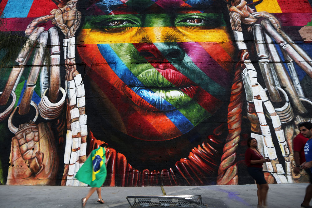 RIO DE JANEIRO, BRAZIL - AUGUST 04: People walk past a section of a mural depicting an indigenous face created by Brazilian graffiti artist Eduardo Kobra and assistants in the revamped Port District on August 4, 2016 in Rio de Janeiro, Brazil. The 32,000-square-foot mural, titled 'We Are All One', was painted to represent cultural diversity across continents. The start of the Rio 2016 Olympic Games on August 5. (Photo by Mario Tama/Getty Images)